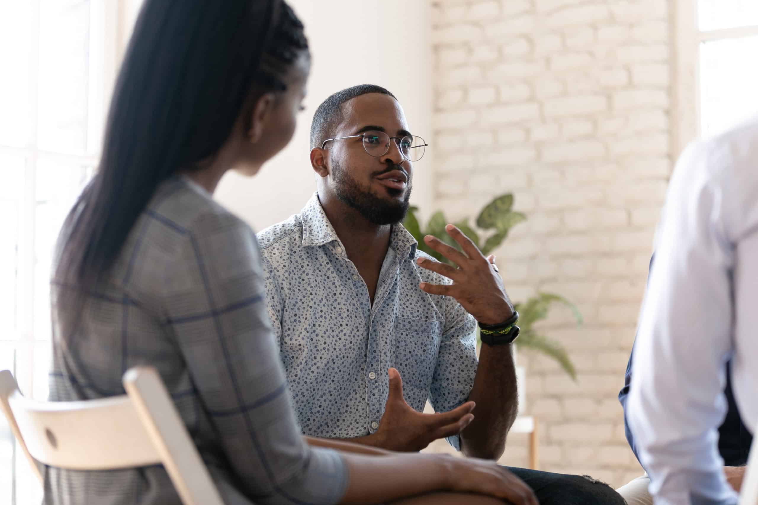 Excited african American man in glasses sit in circle at team therapy session talking sharing thoughts or ideas, motivated biracial male counseling diverse people at group psychotherapy treatment